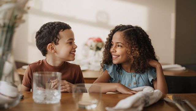 Smiling siblings sharing warm moment at cozy dining table, natural family bond