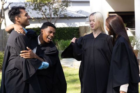 Happy graduates celebrating together outdoors in black academic gowns