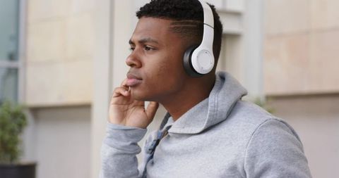 African american man adjusting headphones while listening outdoors in urban hoodie