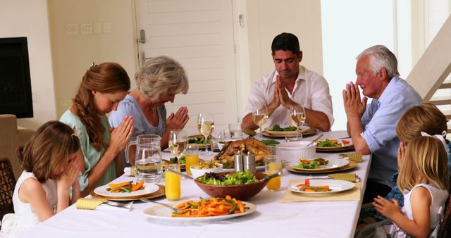 Extended family praying together before dinner at home in the dining room