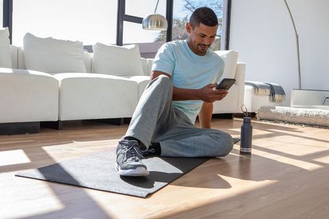 Man Relaxing on Exercise Mat with Smartphone at Home
