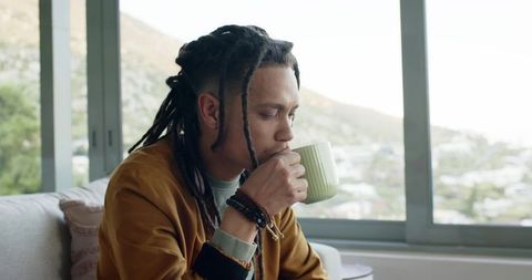 African american man sipping coffee by window with sunlit hillside view
