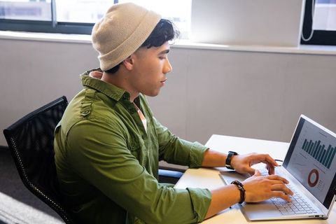 Young man analyzing business charts on laptop at bright modern office desk