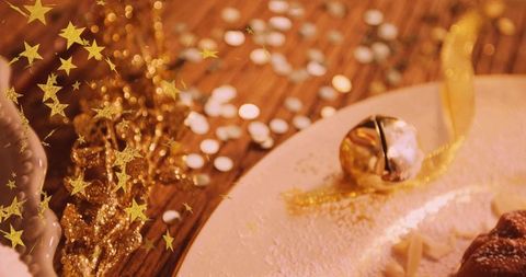 Golden jingle bell on powdered plate with pastry, star confetti and warm holiday bokeh