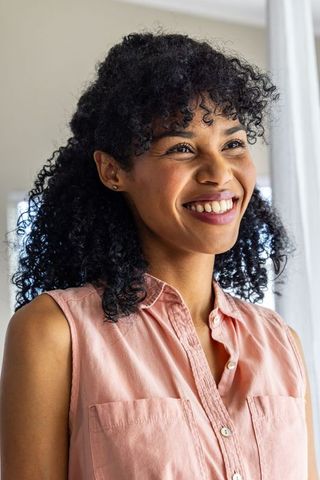 Sunlit smiling woman glancing right wearing pink sleeveless blouse curly hair soft glow