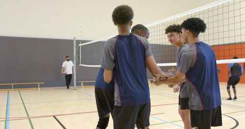 Diverse teenage male volleyball team shaking hands at net in indoor gym
