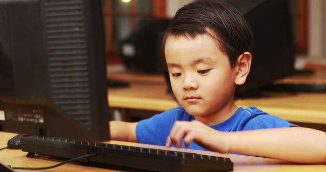 Boy typing on keyboard in computer classroom, focusing intently on screen. Useful for topics related to child education, digital skills development, classroom scenes, modern learning environments, and school technology programs.