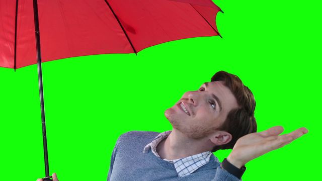 Portrait of a man holding a red umbrella against a vibrant green screen background, smiling while checking for raindrops. This visual can be implemented in weather-related presentations, promotional materials for fashion accessories, film and video editing needing a model with rain gear, or projects involving meteorology-themed content.