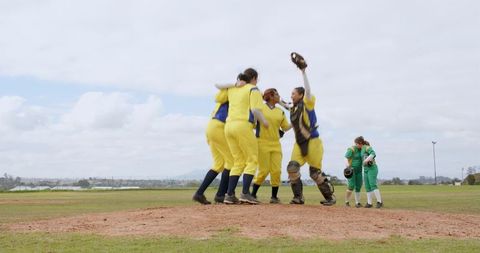 Cheering female softball team huddling on pitcher mound after victory
