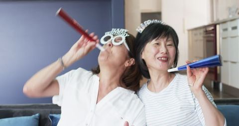Senior multiracial female friends celebrate birthday with joyful noisemakers