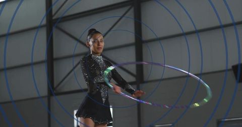 Twirling rhythmic gymnast performing with iridescent hoop in sequined black leotard arena