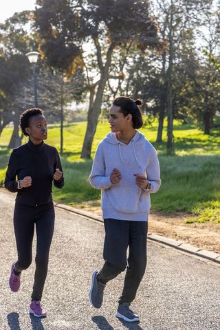 Diverse friends jogging together in urban park wearing wrist fitness trackers, activewear