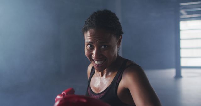 A woman smiling while boxing in a gym, embodying determination and strength. Perfect for promoting fitness, motivation campaigns, sports products, or healthy lifestyle content.