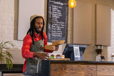 African american barista packing cupcakes into takeout box at cozy cafe