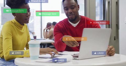Colleagues collaborating at coworking table pointing at laptop with social notifications
