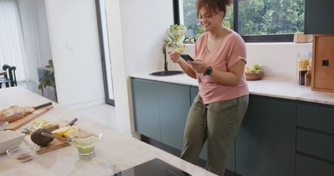 African American woman smiling while checking smartphone in modern kitchen with avocado