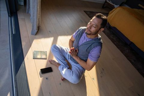 Middle-aged asian man meditating cross-legged near sliding glass door in warm sunlight