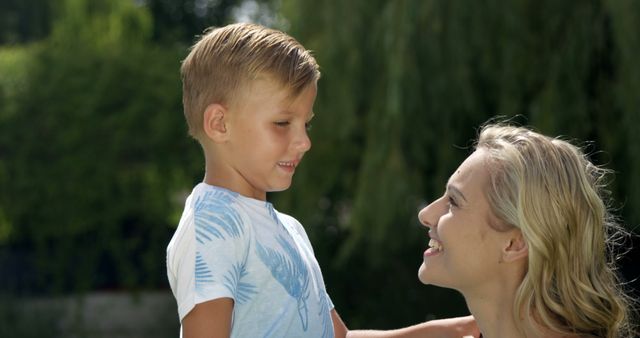 A mother and her young son are enjoying a moment together outdoors. They are smiling at each other, showcasing their bond and happiness. Ideal for articles and advertisements about family time, parenting tips, summer activities, and building strong family relationships.