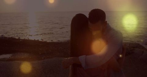 Couple embracing at rocky sunset shoreline with lens flare