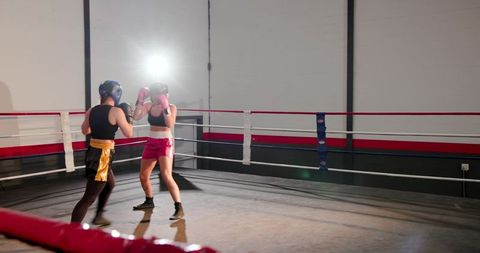 Female boxers sparring under dramatic backlight in gym ring training session