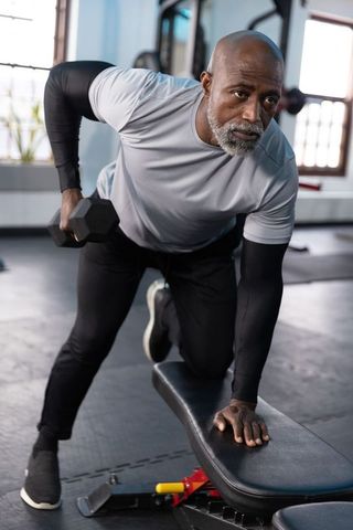 Senior african american man performing one-arm dumbbell row in gym showing strength