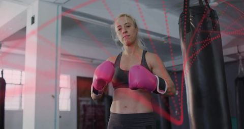 Female boxer training and punching heavy bag with bright pink gloves in industrial gym