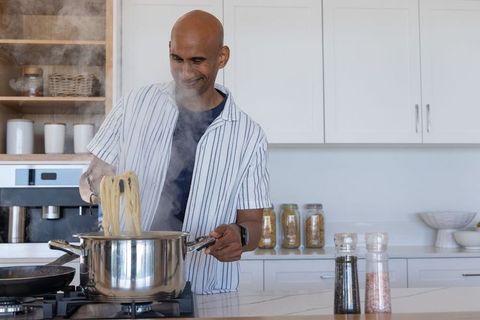 Smiling man cooking spaghetti at modern bright kitchen island with steaming stainless pot