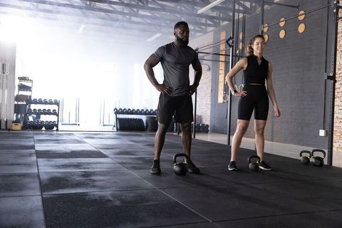 Fitness duo standing with kettlebells in industrial gym, strength training partners