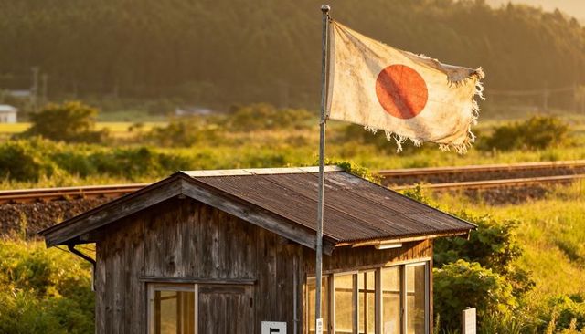 Tattered japanese flag fluttering over rustic wooden hut by railway at golden hour sunset