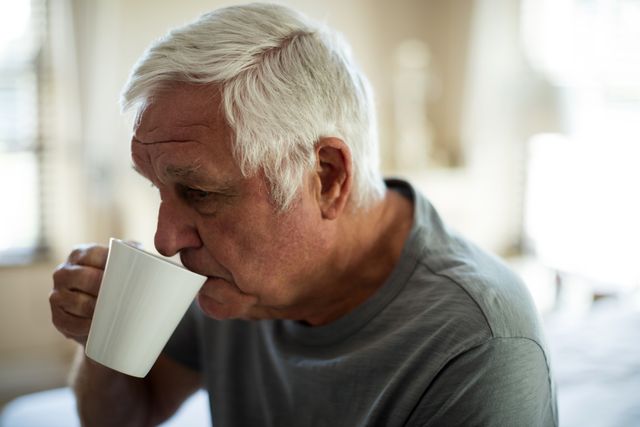 Worried senior man having black coffee in the bedroom at home
