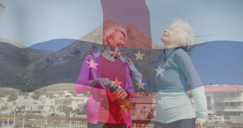 Active senior women laughing on coastal promenade with patriotic flag overlay