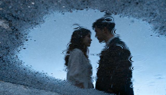 Romantic couple reflected in rain puddle facing each other with raindrop ripples