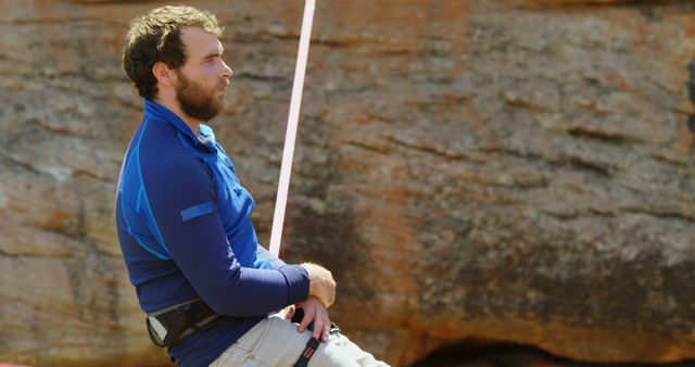 Man engaging in rock climbing, wearing a blue shirt and harness. Perfect for themes related to outdoor adventures, active lifestyles, extreme sports, and training manuals. Useful for advertisements, blog posts, and promotional materials focusing on adventure sports, fitness, and outdoor activities.