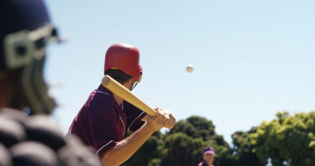 Batter prepares to hit while pitcher throws ball during outdoor baseball game under bright sunlight, suitable for sports articles, advertisements, and team-building presentations