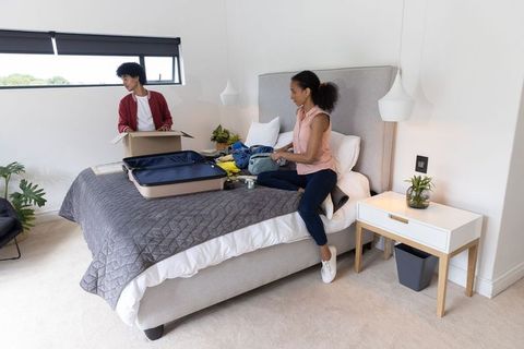 Couple packing and organizing luggage in modern minimalist bedroom preparing for trip