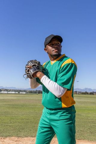 African american baseball pitcher preparing pitch in green uniform on sunny outfield