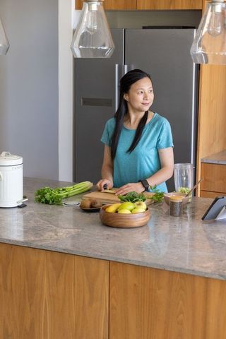 Asian woman chopping salad ingredients at modern kitchen island with tablet and fruit bowl