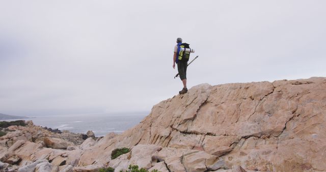 Senior man spending time in nature, standing on rock by seaside admiring the view carrying backpack in slow motion. healthy lifestyle fitness retirement.