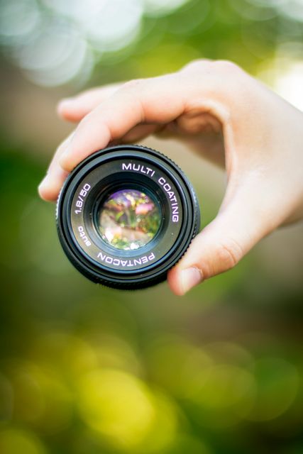 Close-up of Hand Holding Camera Lens Against Blurred Green Background - Download Free Stock Photos Pikwizard.com