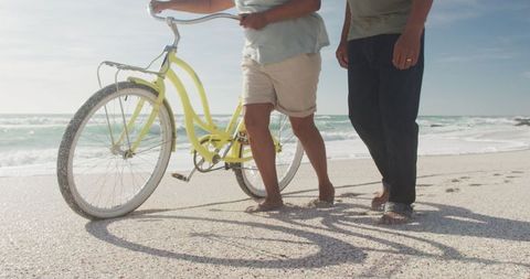 Senior Couple Strolling with Yellow Bicycle on Beach
