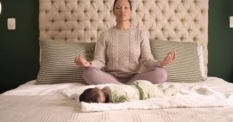 Peaceful mother meditating near sleeping baby in cozy bedroom