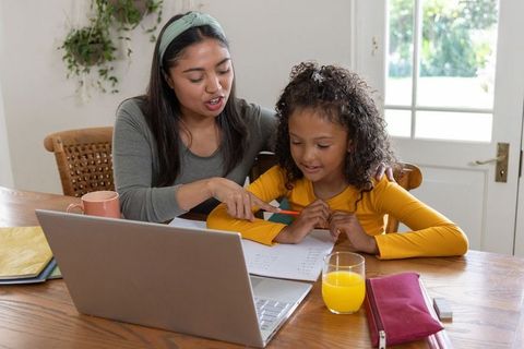 Diverse mother helping daughter with homework at sunlit kitchen table