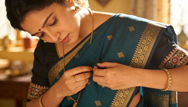 Woman adjusting teal-blue sari fastening safety pin close-up, embroidered gold border, bindi
