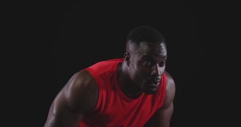 Muscular man leaning forward pushing through fatigue in red sleeveless top intense focus