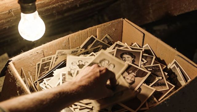 Sifting vintage family portraits from dusty cardboard box in attic under exposed bulb