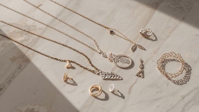 Sunlit gold and silver jewelry flatlay on beige marble — necklaces rings bangle
