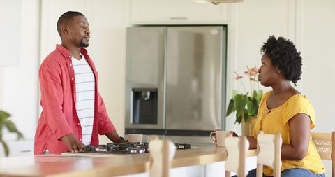 African american couple chatting at kitchen island holding mugs in bright modern home
