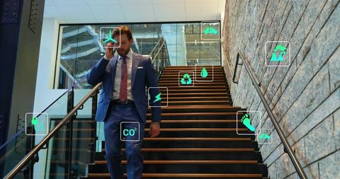 Executive walking down office stairs talking on phone with sustainability icons overlay