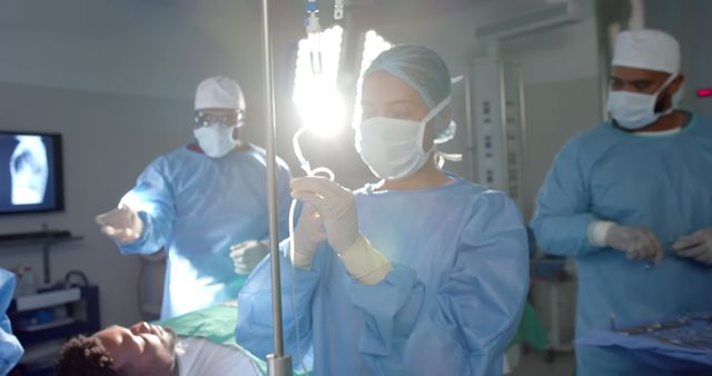 A surgical team is performing a medical procedure in an operating room. The healthcare professionals, including doctors and nurses, are wearing blue sterile gowns and surgical masks. One member is adjusting a surgical light while others are focused on the patient lying on the operating table. This image can be used for medical articles, healthcare promotions, hospital websites, or educational materials on surgical procedures and healthcare professions.