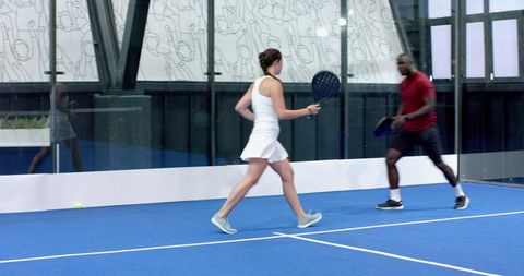 Competitive Athletes Engaged in Dynamic Padel Match on Glass Court
